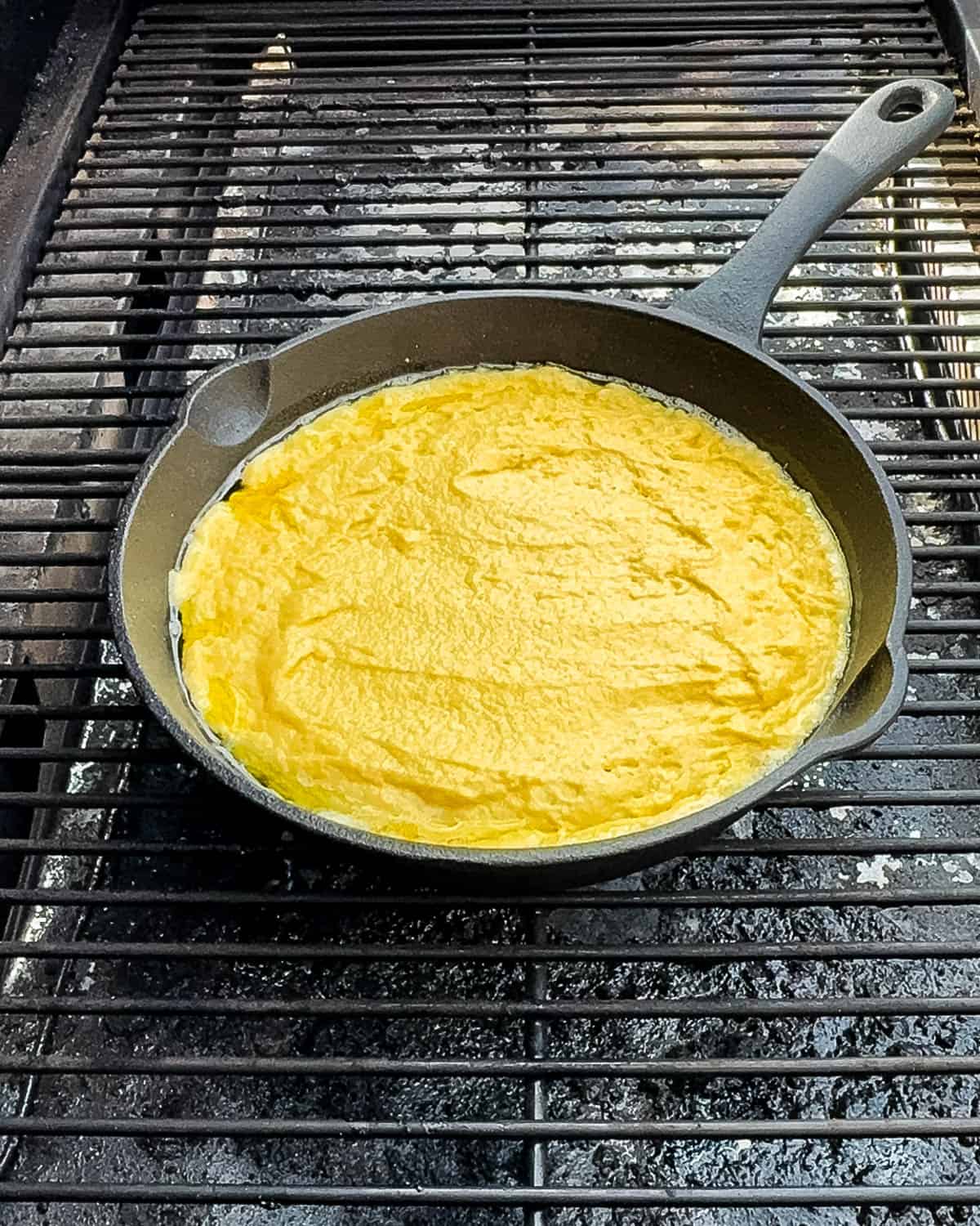 Spreading cornbread batter evenly in buttered cast iron skillet.