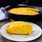 Buttery smoked cornbread in hot cast iron pan fresh off the smoker with one piece removed and placed on a plate.