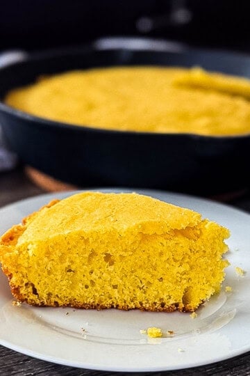 Buttery smoked cornbread in hot cast iron pan fresh off the smoker with one piece removed and placed on a plate.