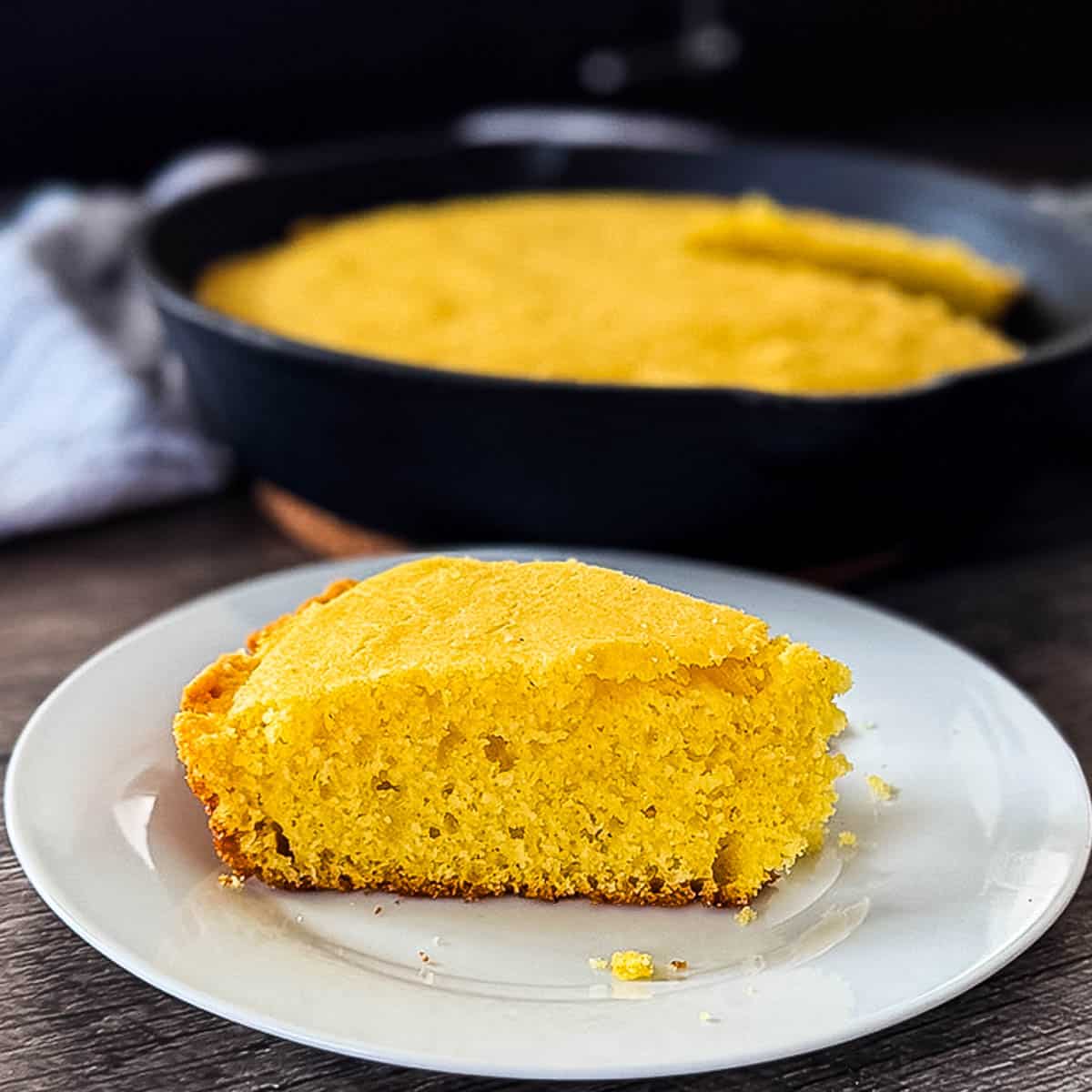 Buttery smoked cornbread in hot cast iron pan fresh off the smoker with one piece removed and placed on a plate.