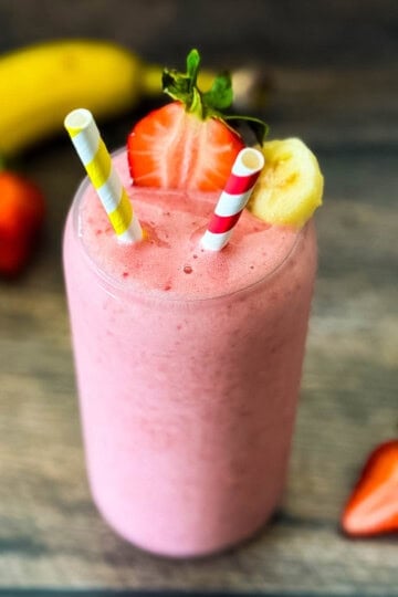 Strawberry banana smoothie in a clear glass with two straws.