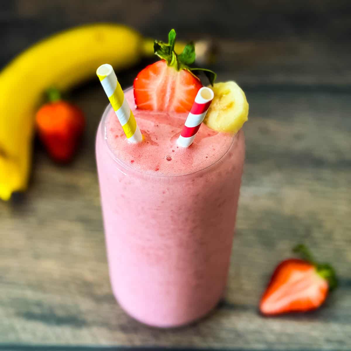 Strawberry banana smoothie in a clear glass with two straws.