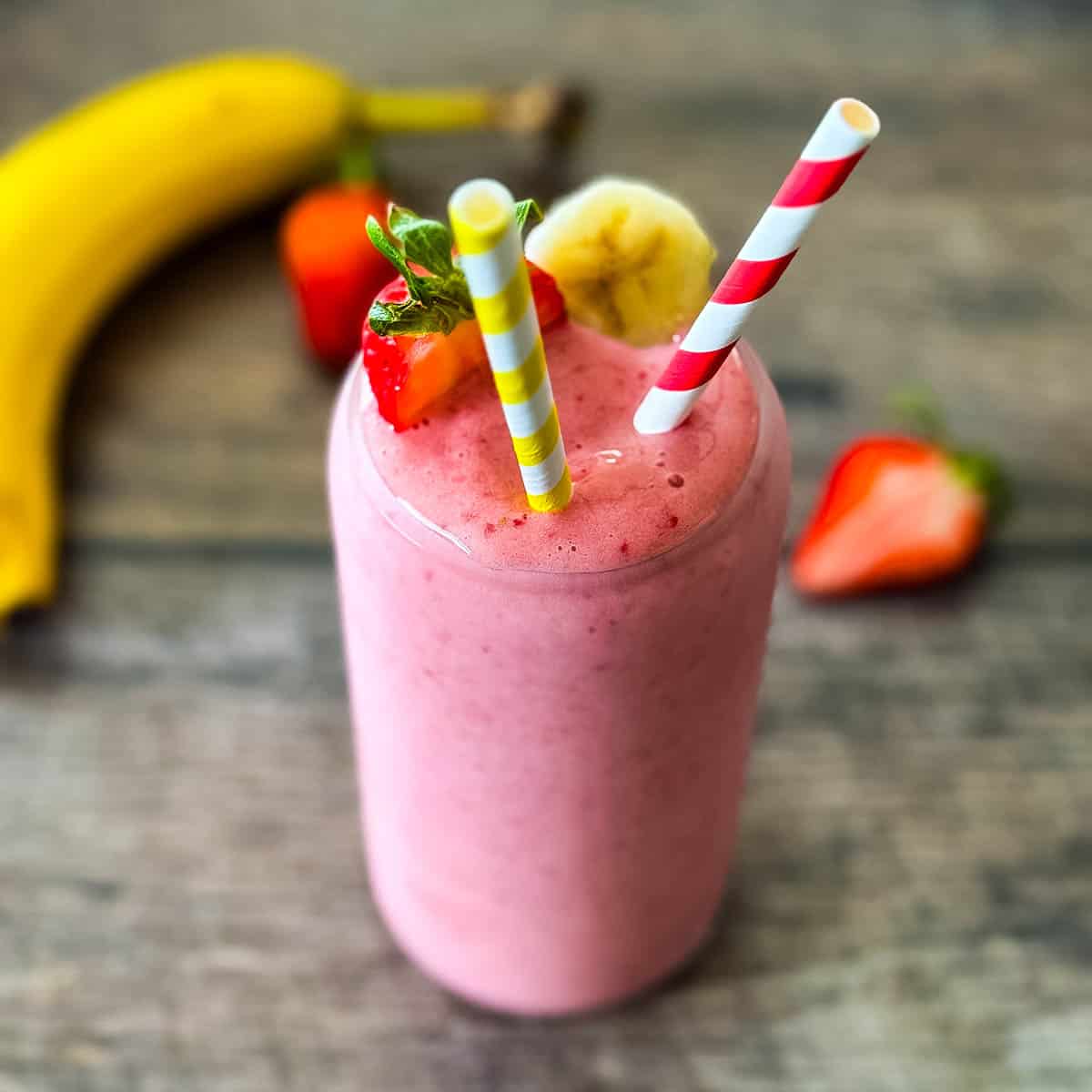 Strawberry banana smoothie in a glass with a fresh strawberry garnish.