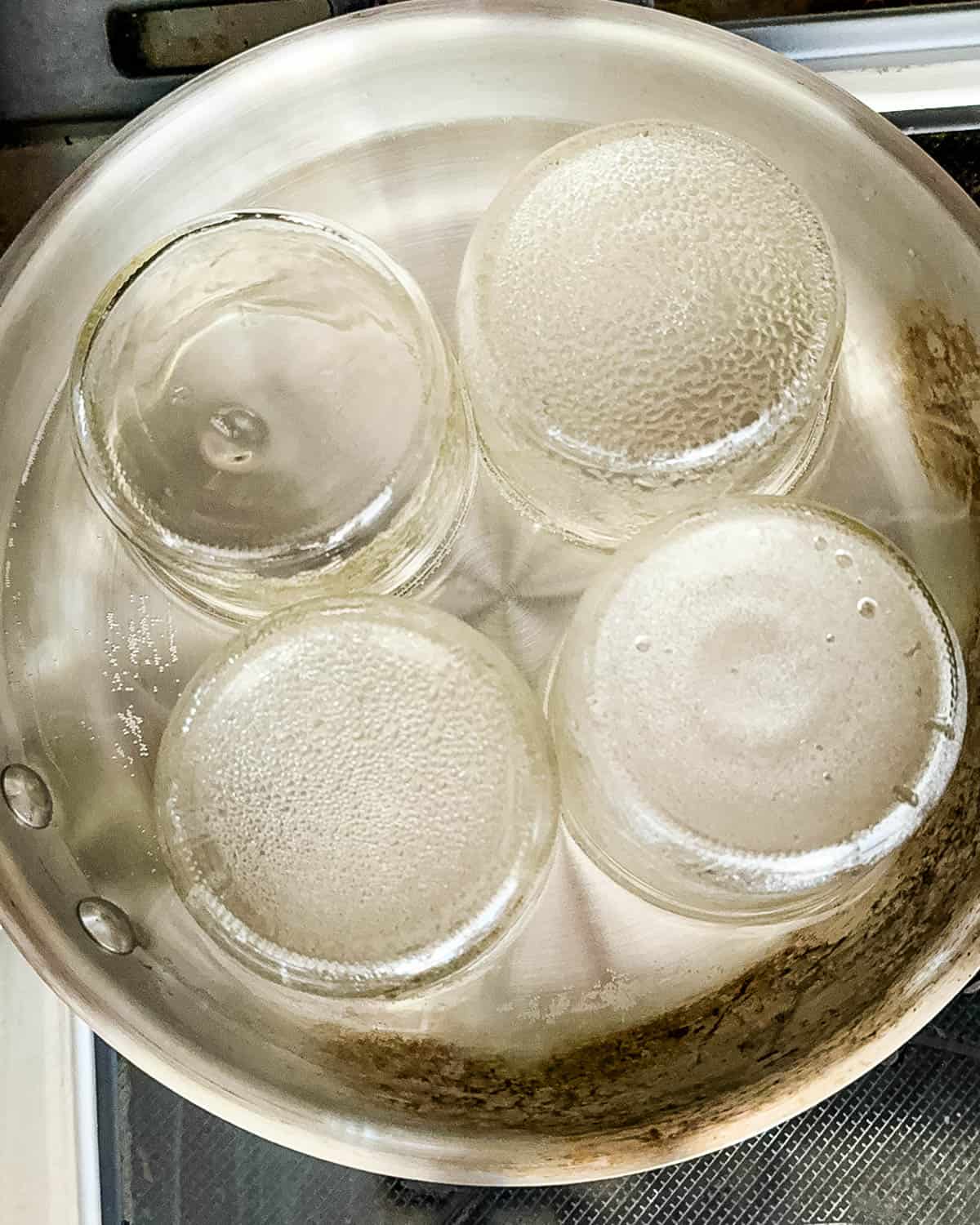 Glass canning jars simmering upside down in a pot of hot water to sterilize before filling.
