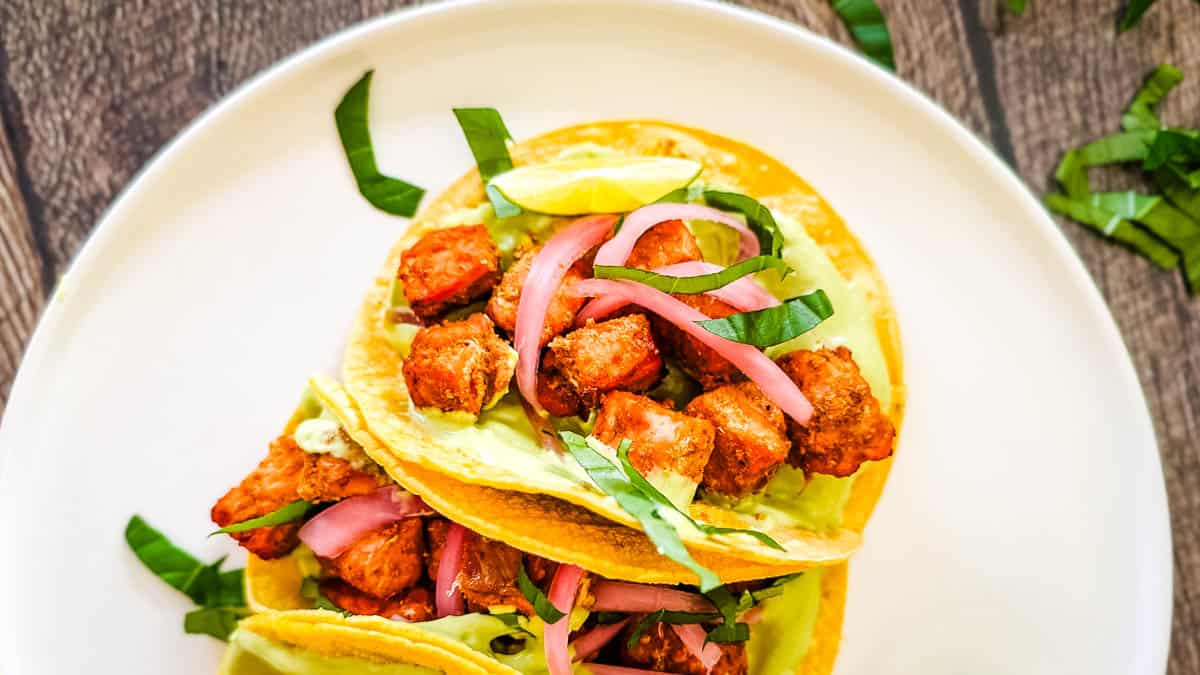 Crispy salmon tacos stacked on a plate with avocado crema, pickled onions, and fresh herbs, ready to serve.