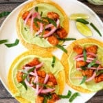 Air fryer salmon tacos on corn tortillas topped with avocado lime crema, pickled red onions, and fresh cilantro, served with lime wedges on a white plate.