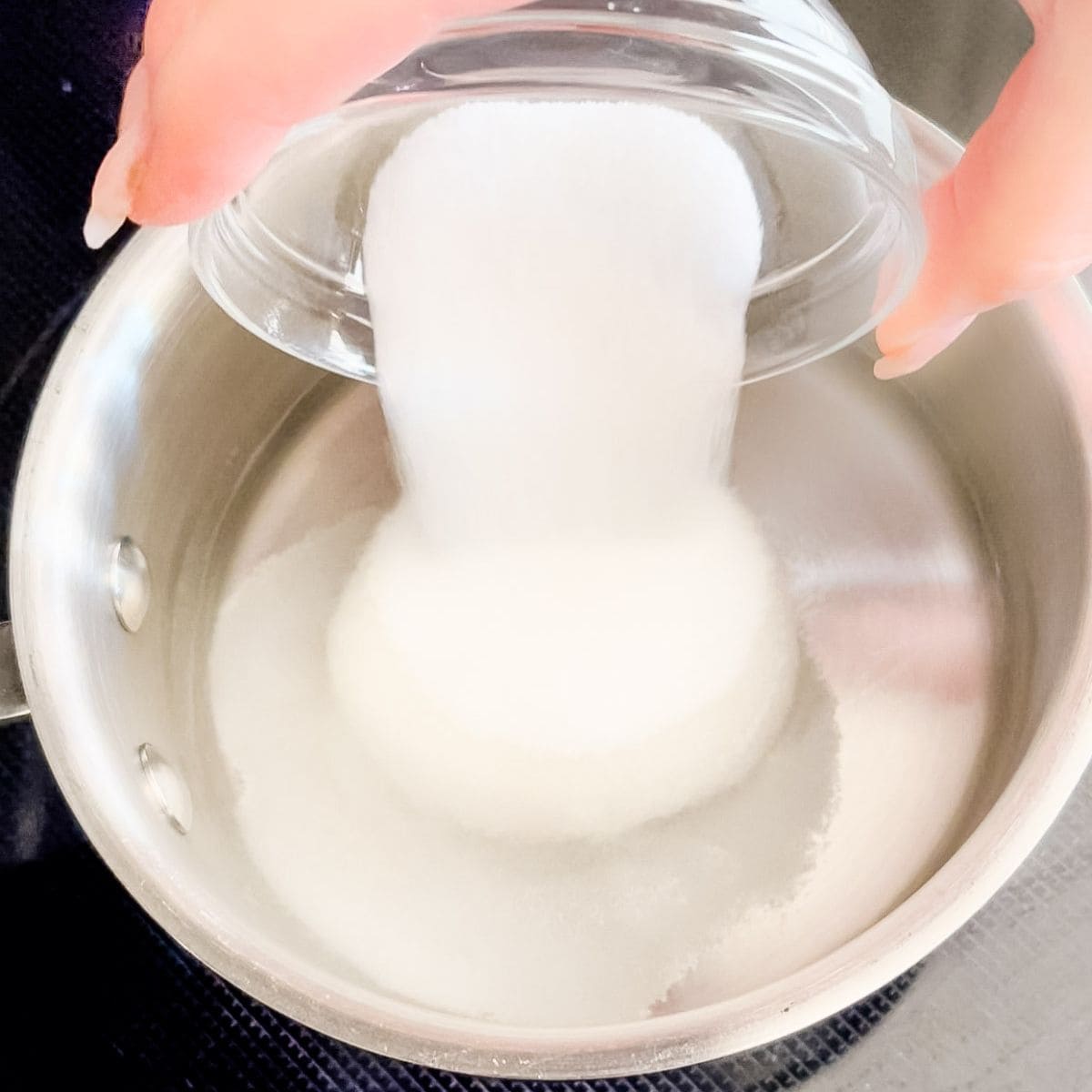 White sugar being poured into a small saucepan with water.