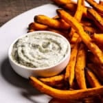 Crispy sweet potato fries served with creamy homemade dill mayo sauce in a small white bowl.