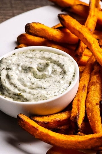 Crispy sweet potato fries served with creamy homemade dill mayo sauce in a small white bowl.