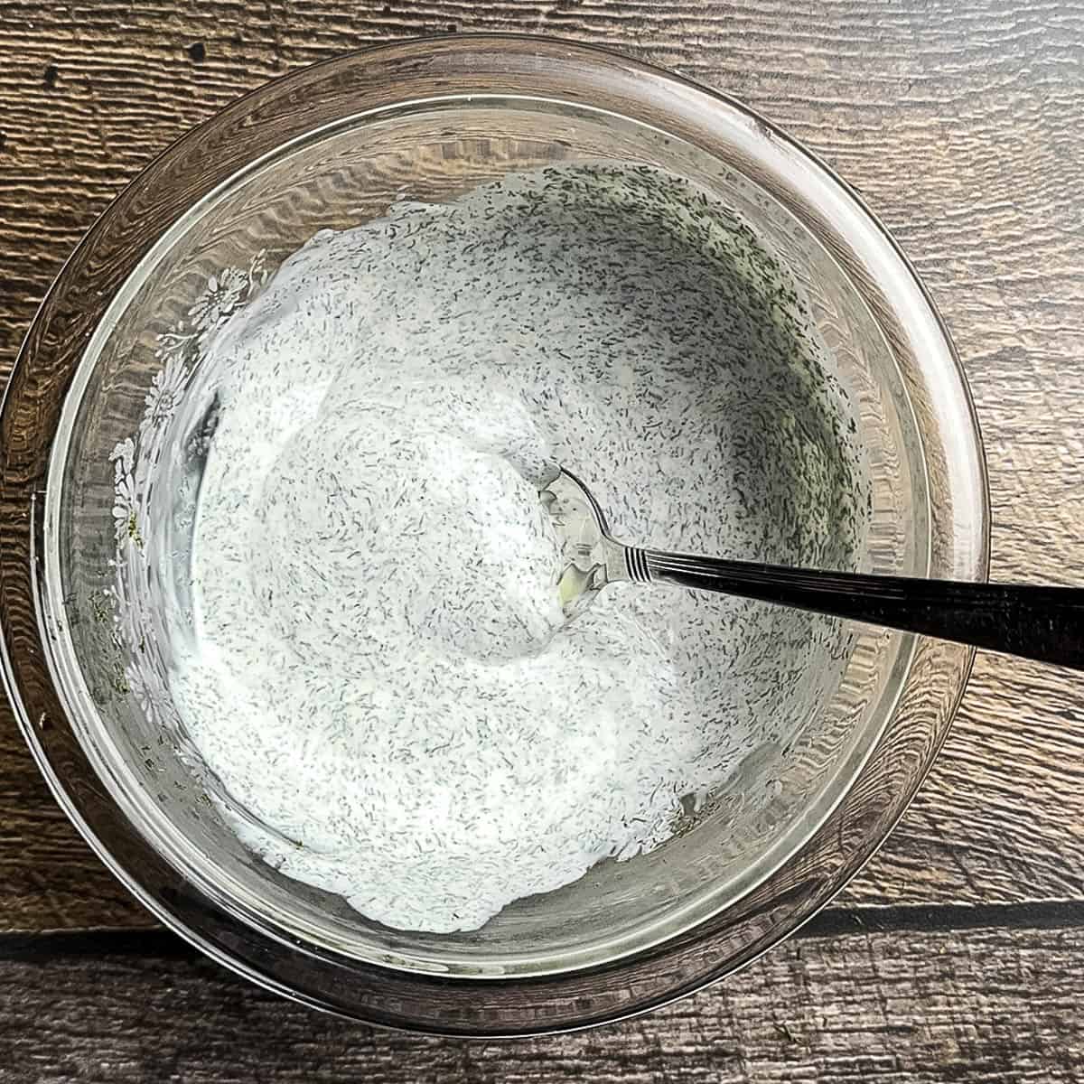 Creamy homemade dill sauce mixed in a glass bowl with a spoon, ready to chill and serve.