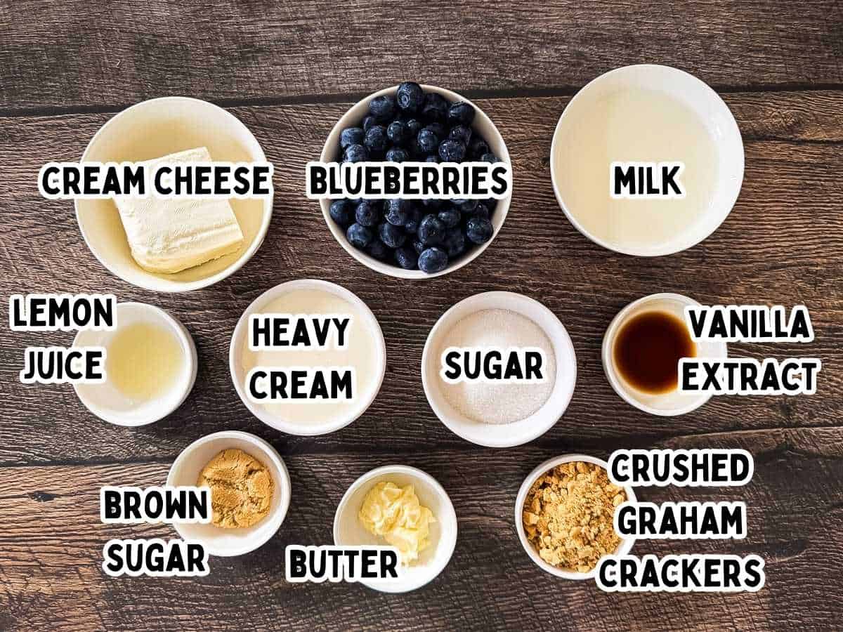 Labeled ingredients for Ninja Creami blueberry cheesecake ice cream laid out on a counter, including cream cheese, blueberries, milk, cream, sugar, and graham crackers.