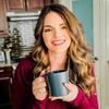 Jeri Walker in her kitchen smiling and holding a cup of coffee.