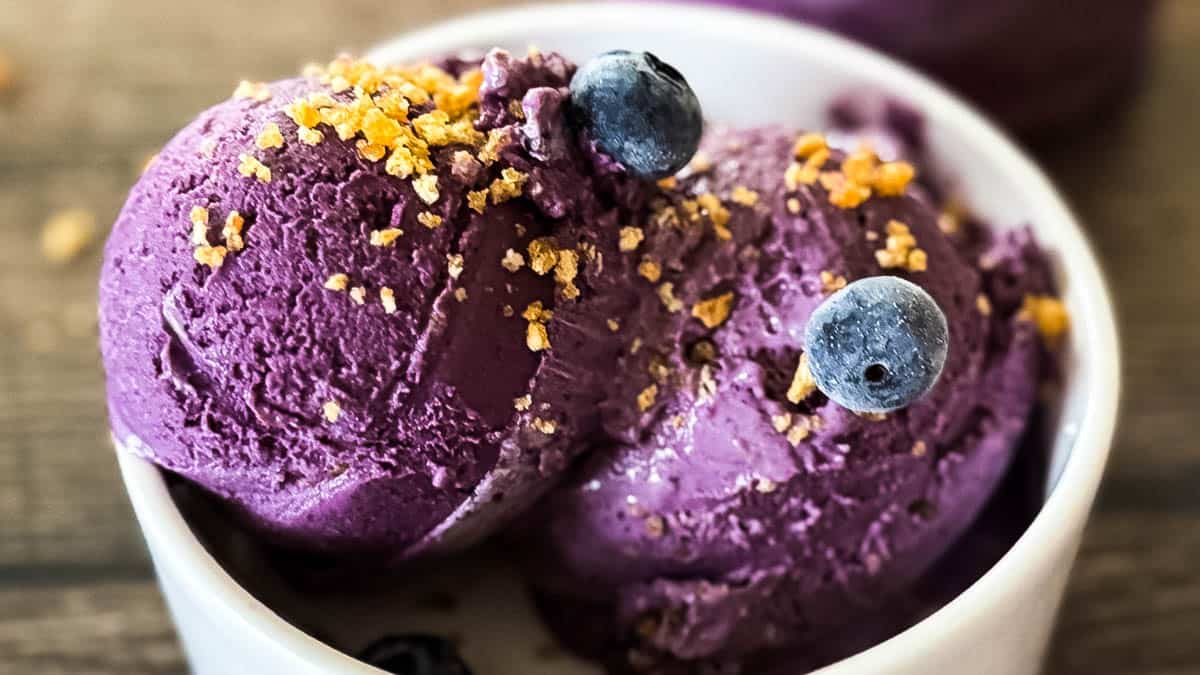 Creamy blueberry cheesecake ice cream in a white bowl, topped with leftover graham cracker mixture.