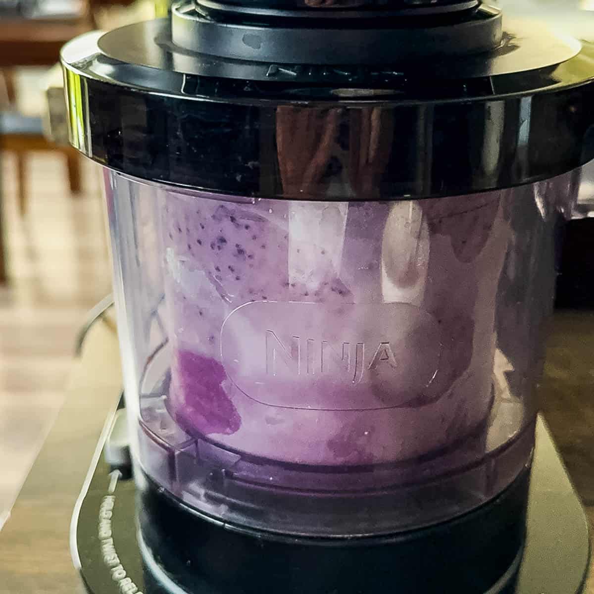 Frozen blueberry cheesecake ice cream base in a Ninja Creami machine during the first spin.
