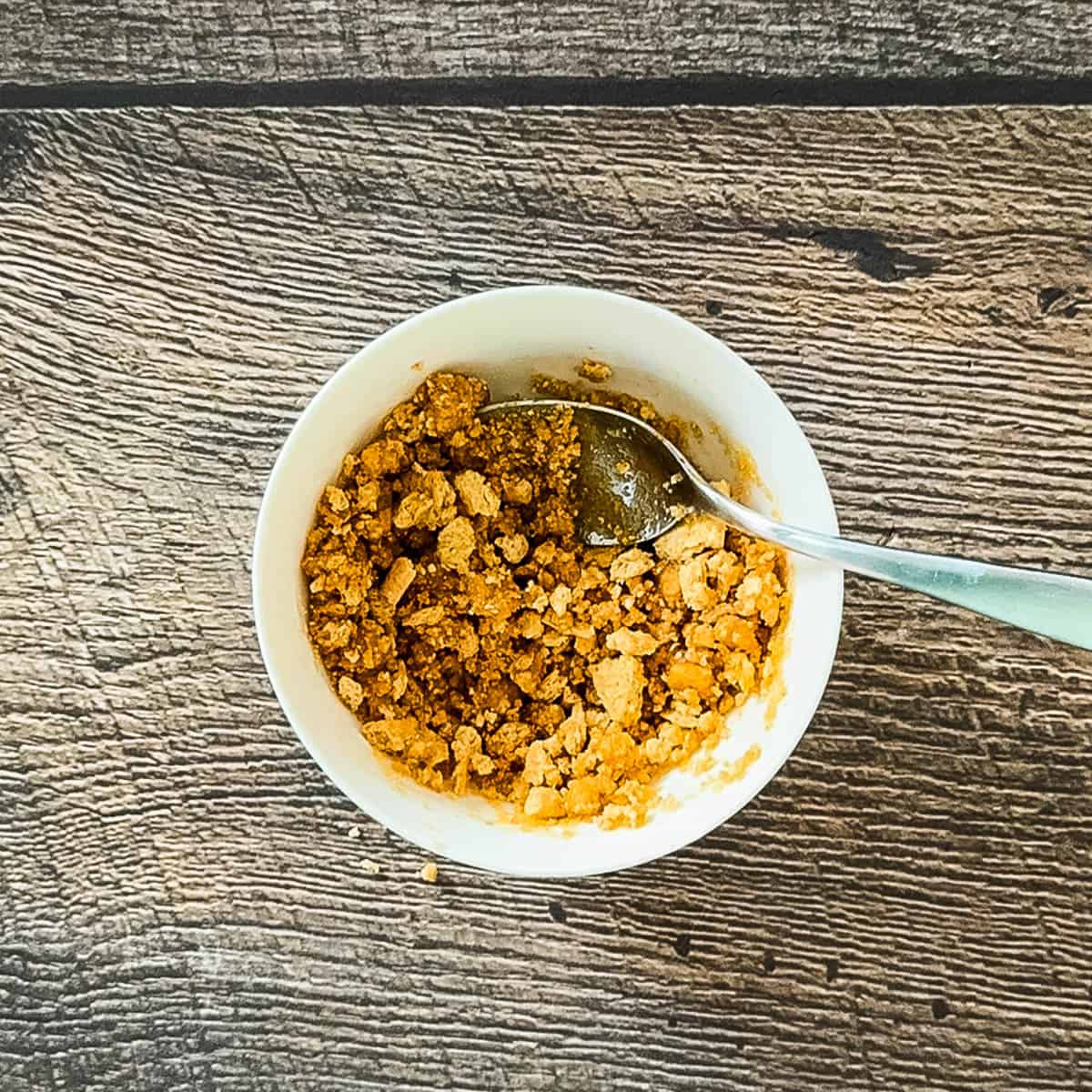 Graham cracker crumbs mixed with melted butter and brown sugar in a small bowl.