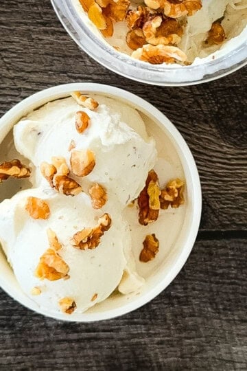 Two scoops of maple walnut ice cream in a white bowl, topped with toasted walnuts.