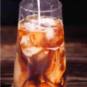 Tall glass of iced coffee swirling with cream, sitting on a burlap napkin with coffee beans, with text overlay that reads “How to Make the Best Iced Coffee” from Winding Creek Ranch.