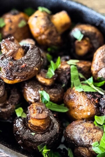 Mushrooms piled in a cast iron dish, topped with chopped fresh basil for garnish.
