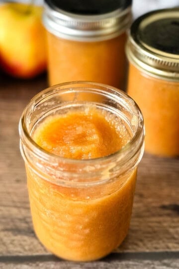 Homemade canned applesauce in a glass jar, with more jars and apples in the background.