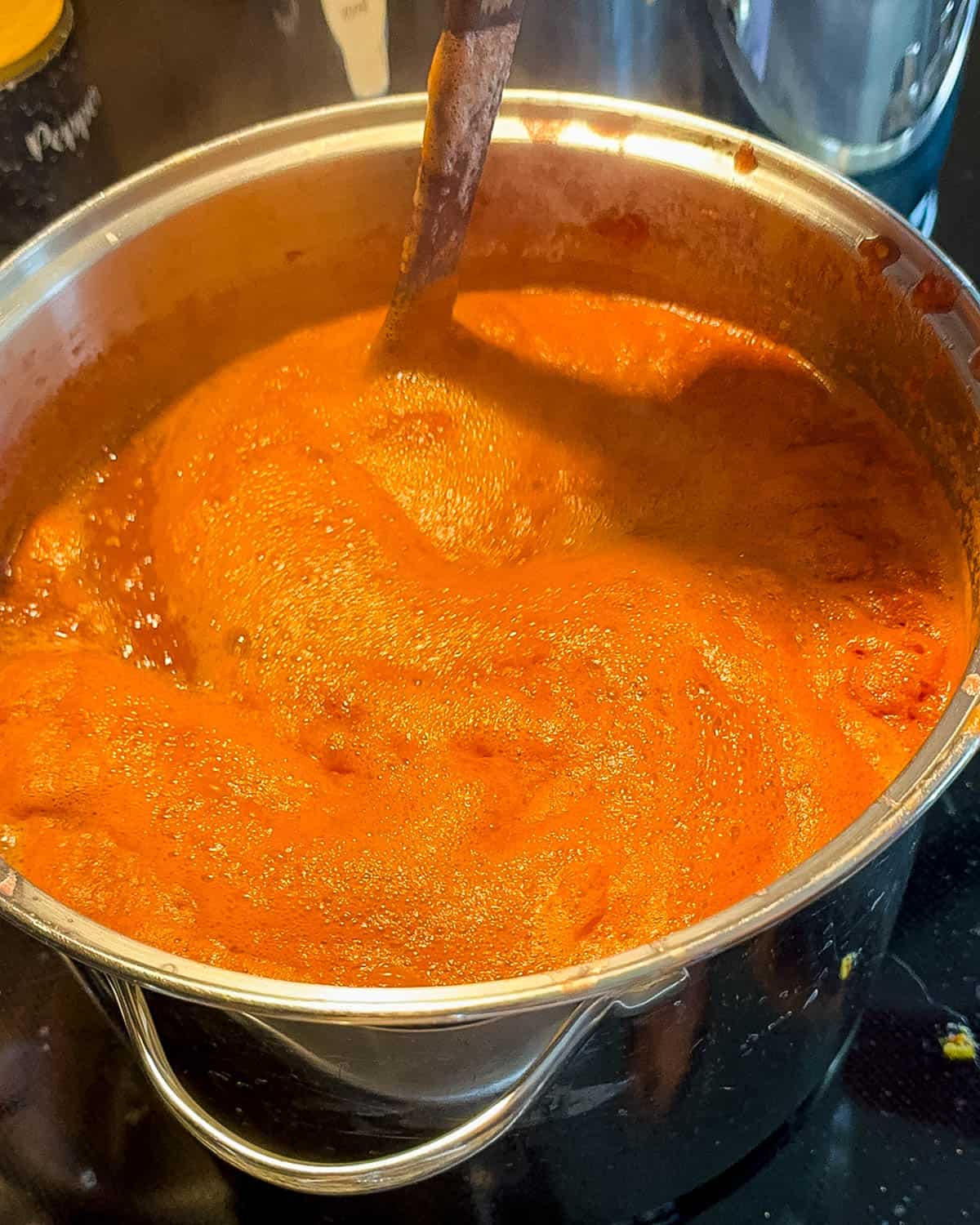 A large pot of salsa simmering on the stove, being stirred with a wooden spoon.