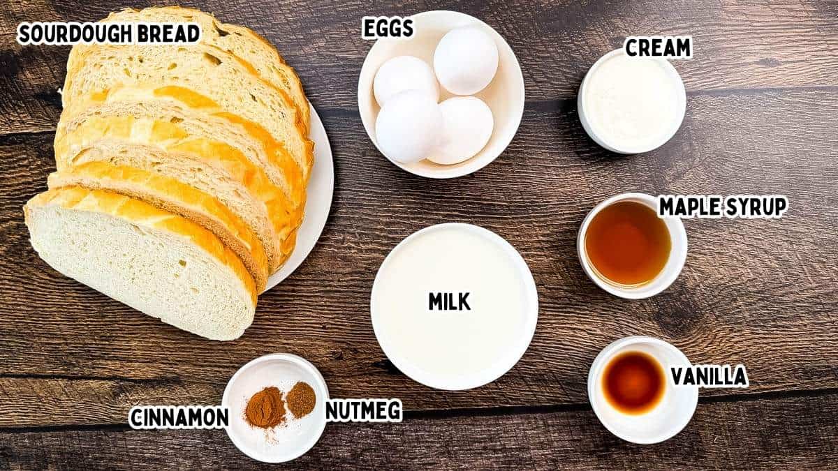 Labeled ingredients for sourdough french toast, including sourdough bread slices with eggs, milk, maple syrup, vanilla, cinnamon, nutmeg, and cream on wooden table.