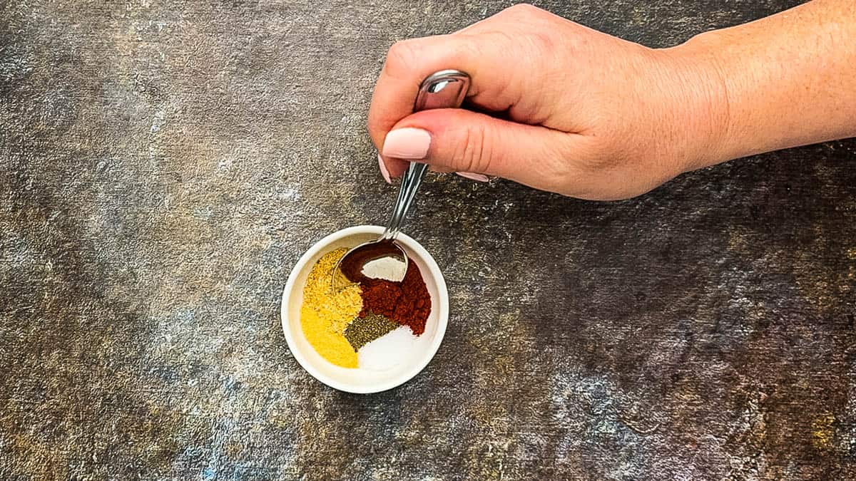 Hand mixing pork spice rub ingredients in a small white dish.