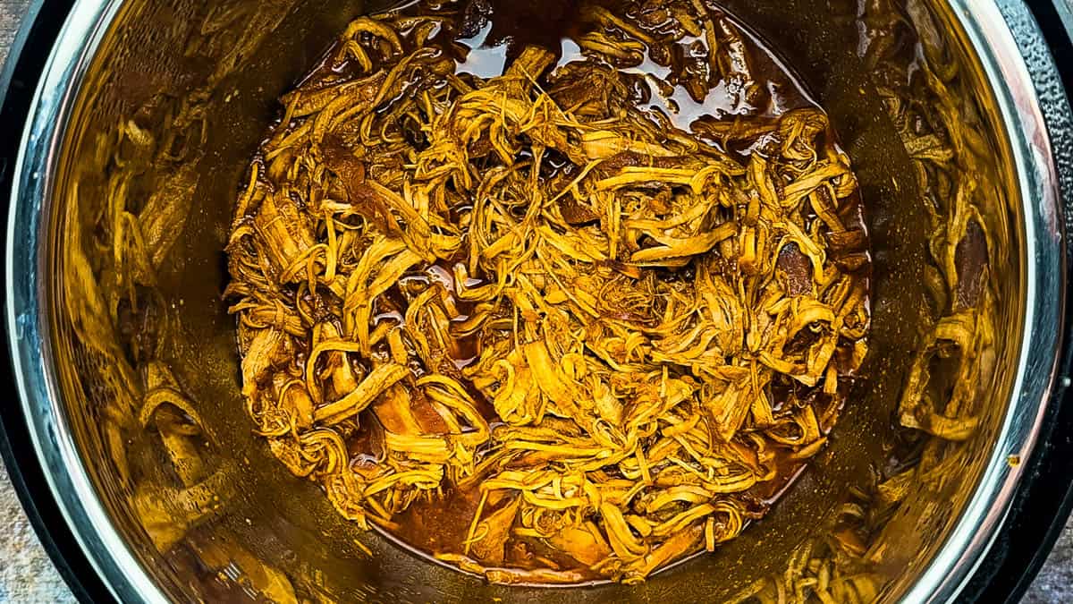 Shredded BBQ pulled pork tenderloin mixed with sauce inside the Instant Pot.