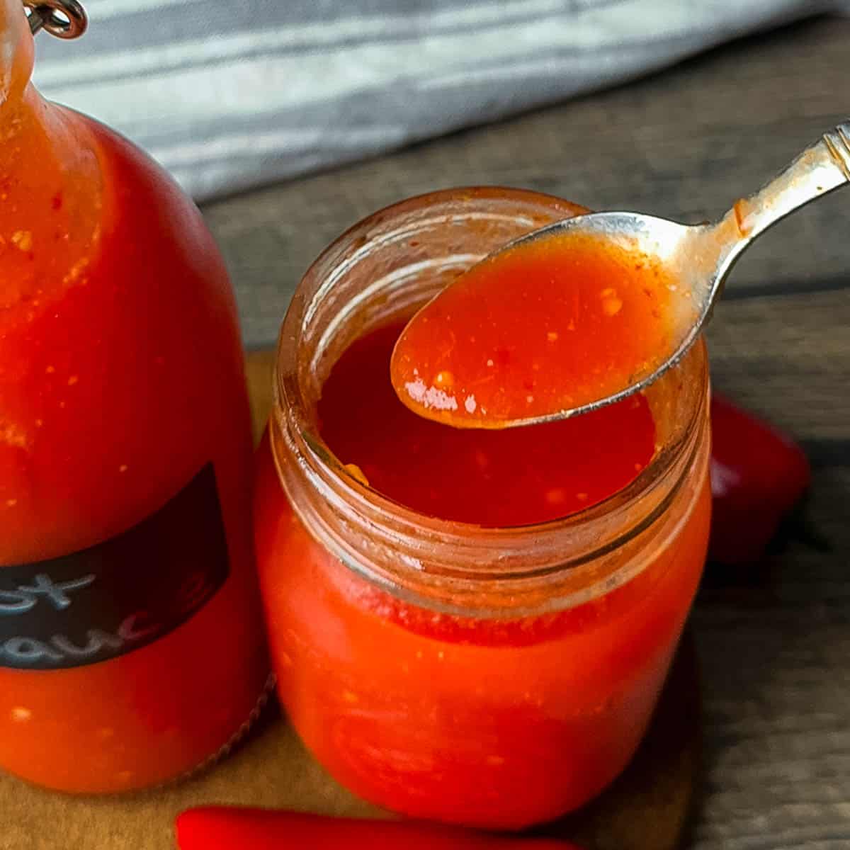 A spoonful of homemade hot sauce being lifted from an open jar, showing its smooth texture.