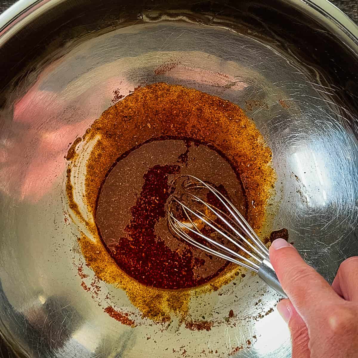 A hand whisking spice rub mixture in large bowl.
