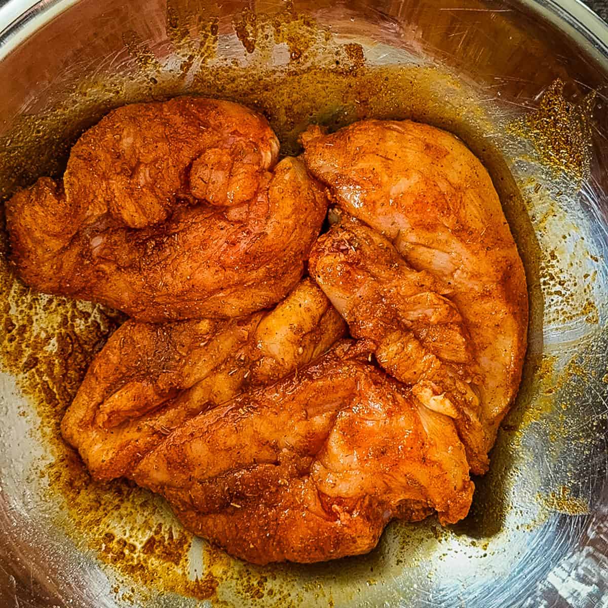 Chicken breasts in large bowl, covered evenly in spice mixture.
