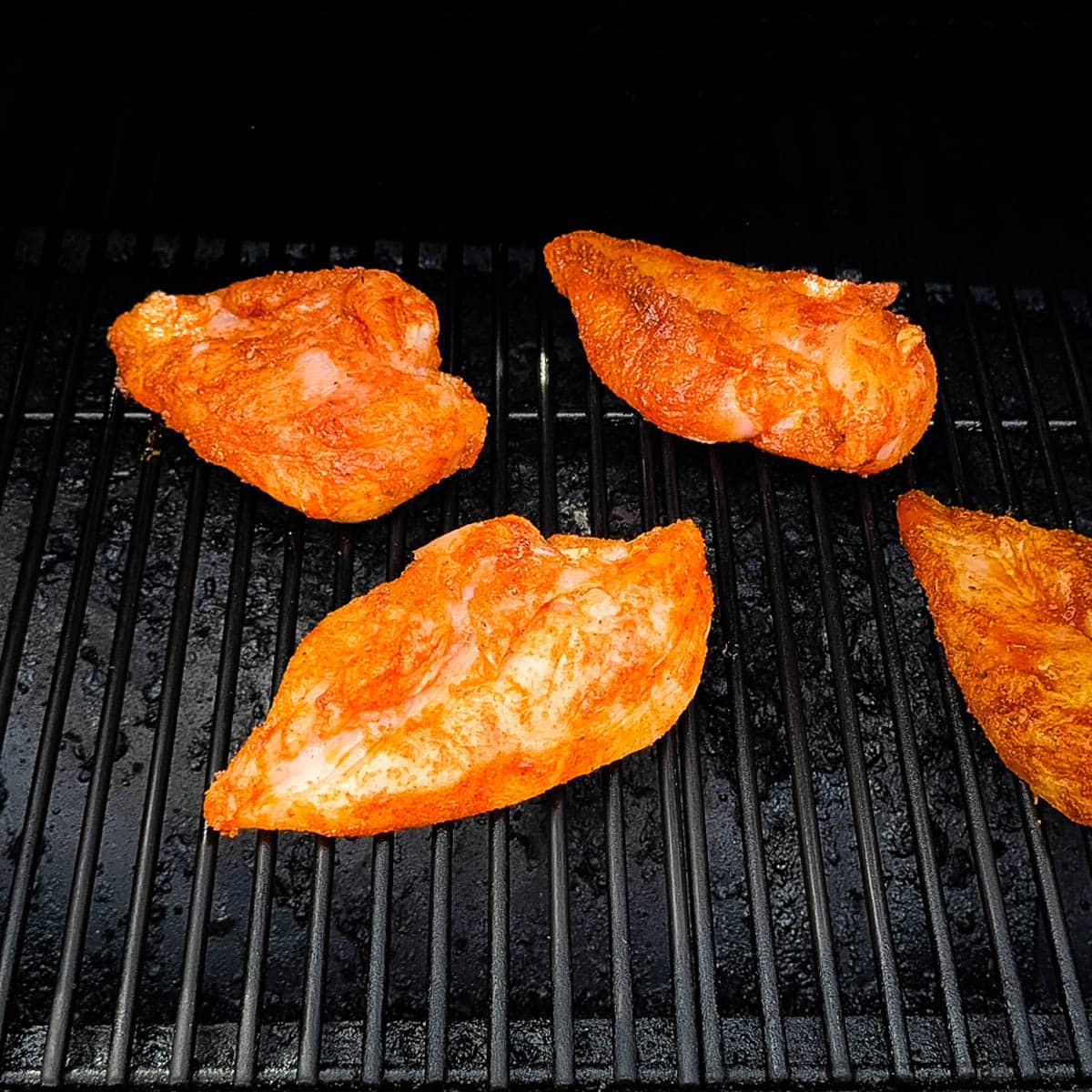 Seasoned chicken breasts placed on grill grates of pellet grill.