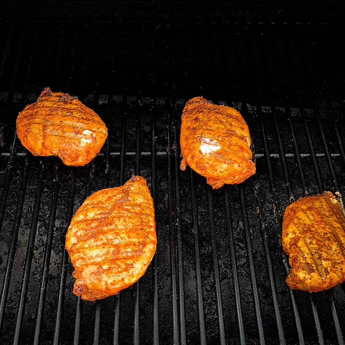 Cooked chicken breasts on the grill grates of smoker.