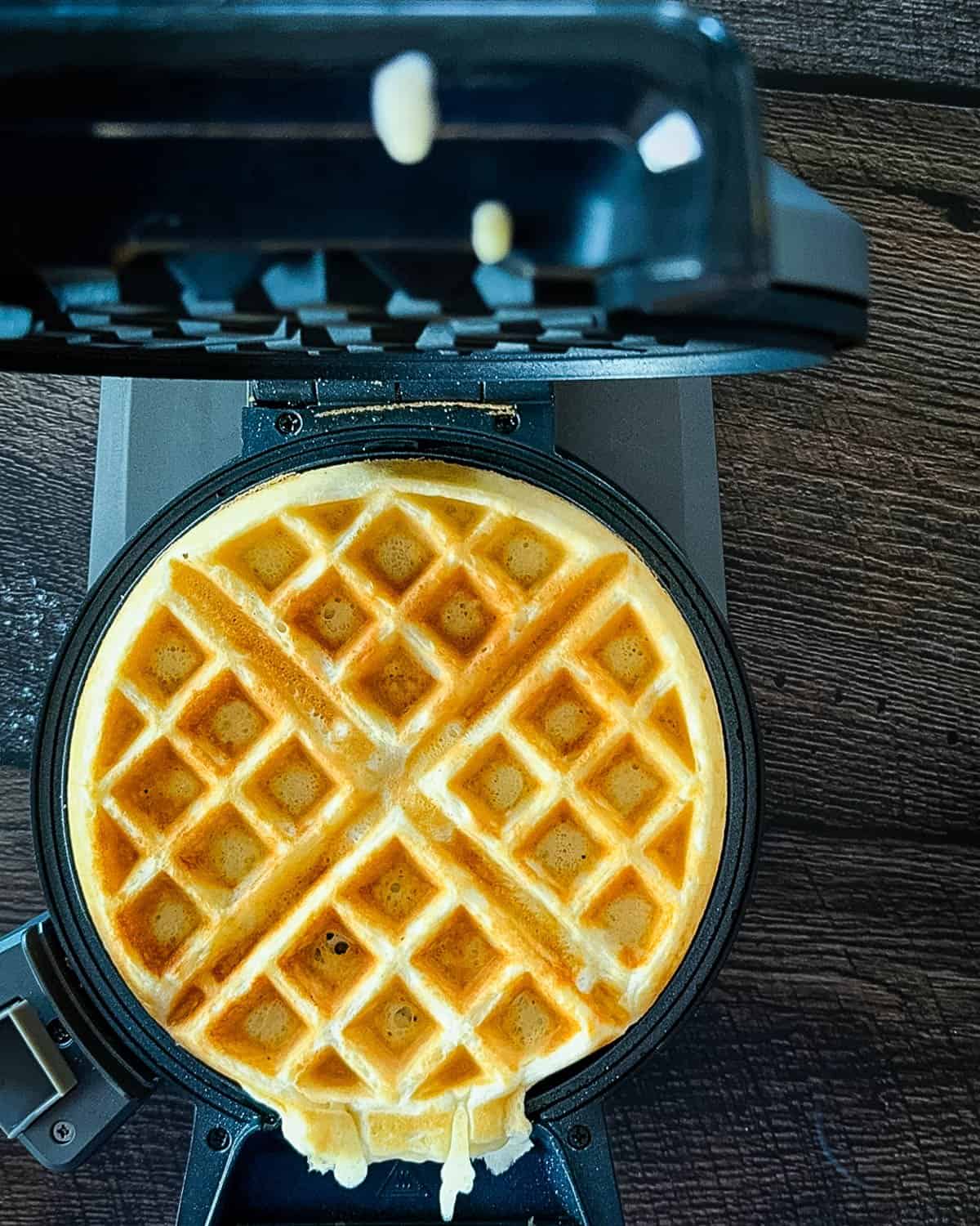 Golden waffle finished cooking in a waffle iron with crisp edges.