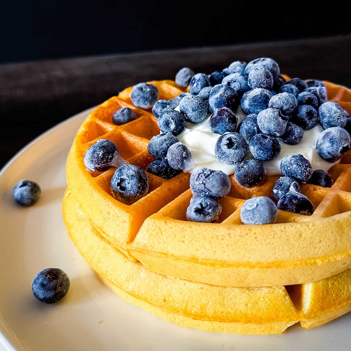 Stack of sourdough discard waffles topped with yogurt and fresh blueberries on a white plate.