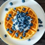 Golden sourdough discard waffle topped with yogurt and fresh blueberries on a white plate.