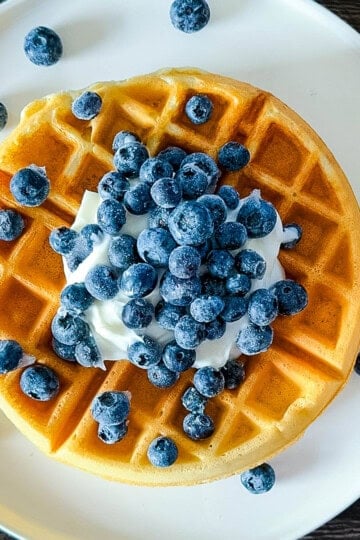 Golden sourdough discard waffle topped with yogurt and fresh blueberries on a white plate.
