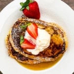 Fresh strawberry-topped sourdough French toast with whipped cream and powdered sugar.