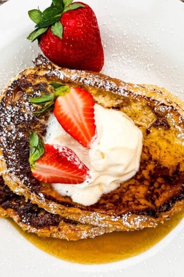 Fresh strawberry-topped sourdough French toast with whipped cream and powdered sugar.