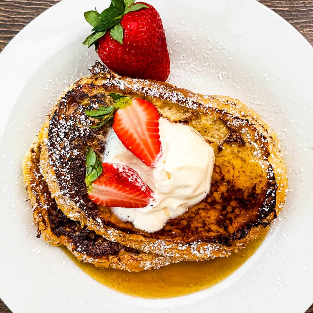 Fresh strawberry-topped sourdough French toast with whipped cream and powdered sugar.