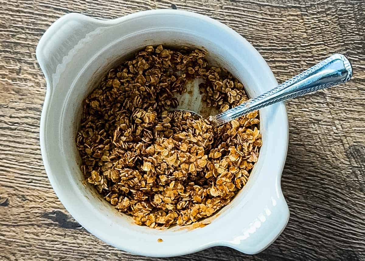 Oat crumble topping mixture with brown sugar, oats, butter, and cinnamon in a white bowl with a spoon.