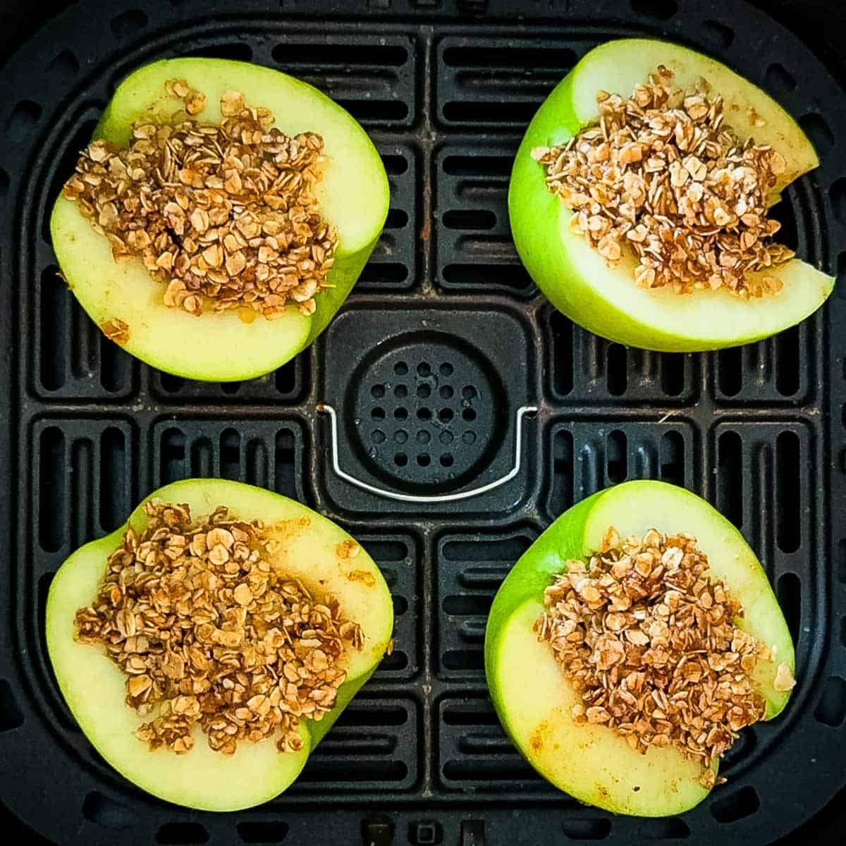 Uncooked apple halves filled with oat crumble arranged in a single layer in an air fryer basket.