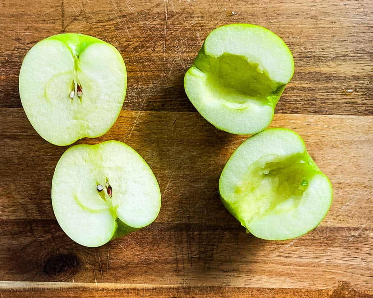Halved and cored green apples on a wooden cutting board, ready to be filled for air fryer baked apples.