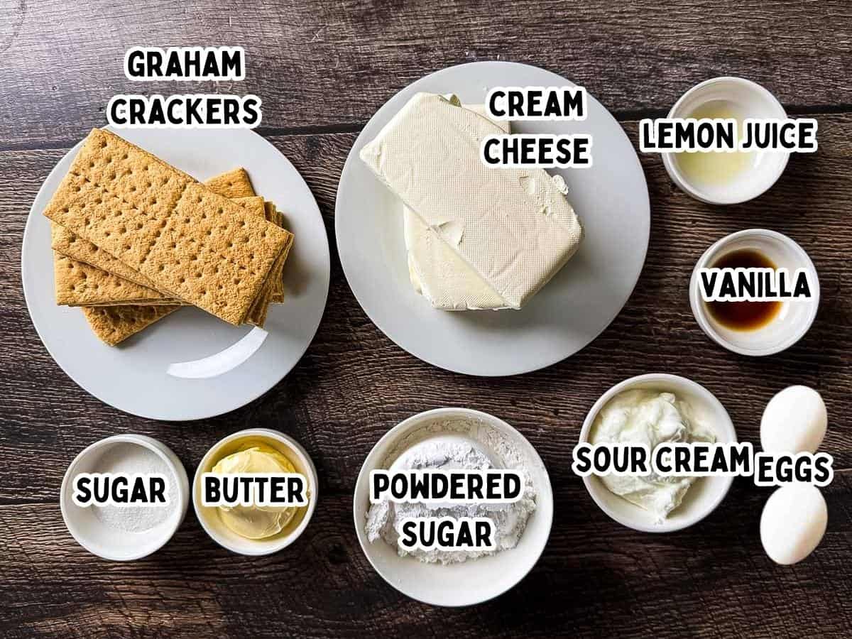 Labeled ingredients for smoked cheesecake in small white dishes on a wooden table.