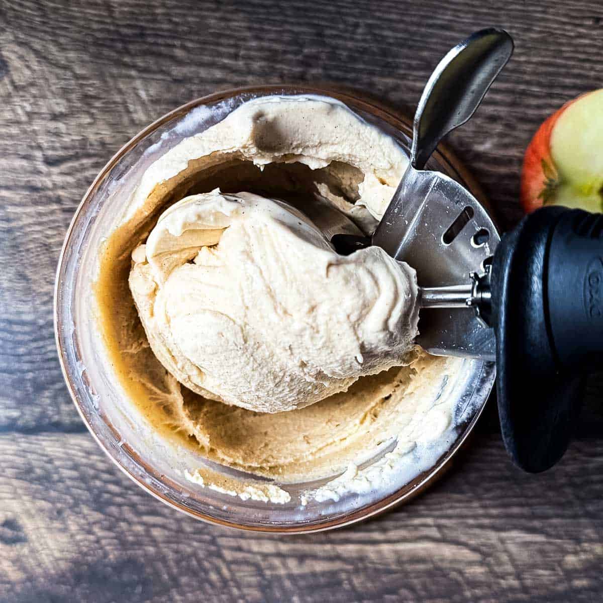 An ice cream scoop scooping up a scoop of apple pie ice cream.