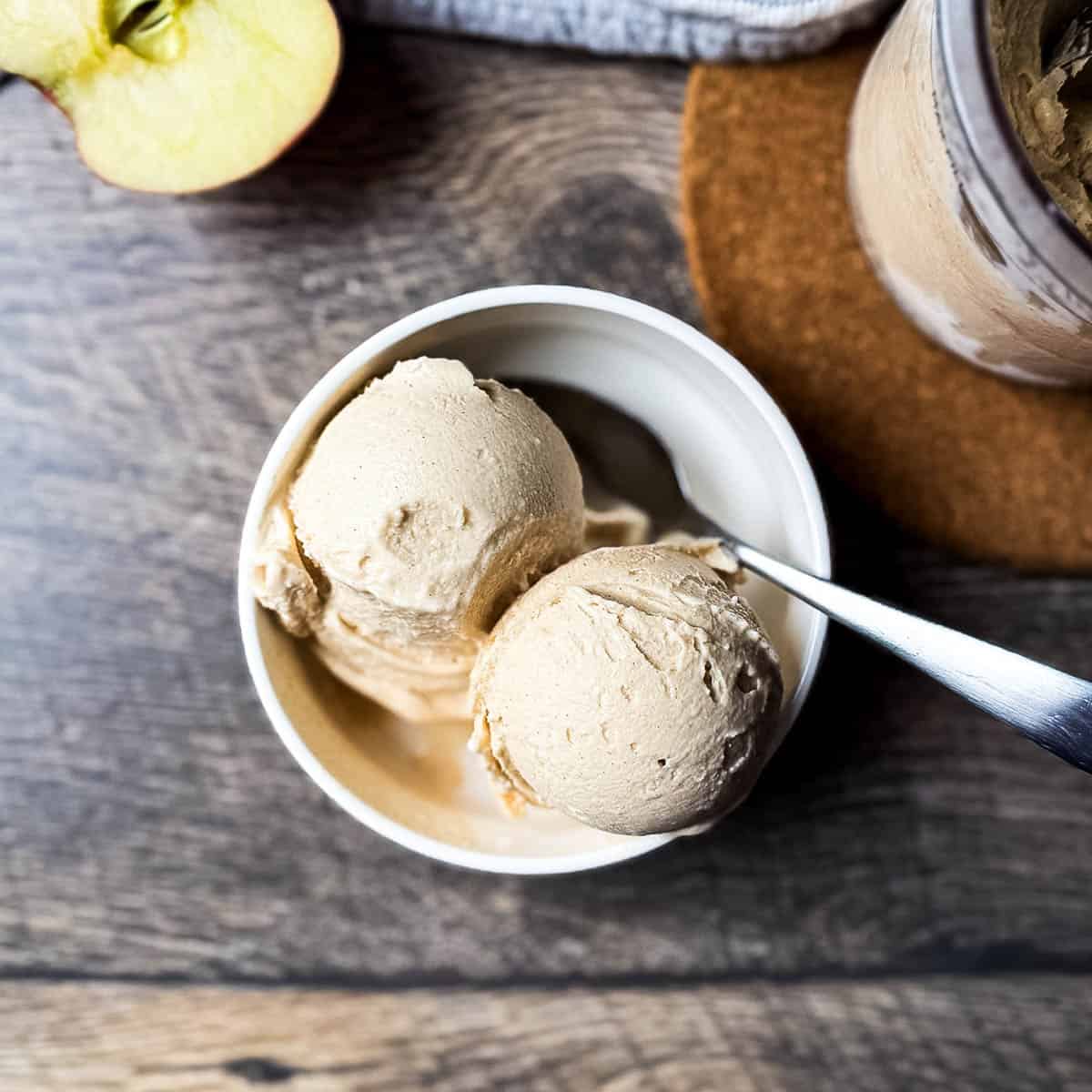 Overhead view of two scoops of apple pie ice cream in a bowl, next to the Ninja Creami frozen pint container.