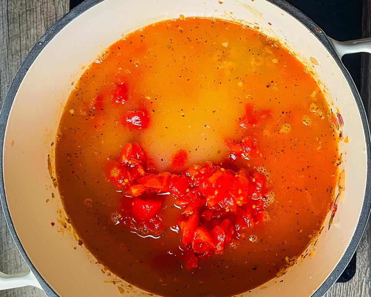 Chicken broth and diced tomatoes added to the soup pot.