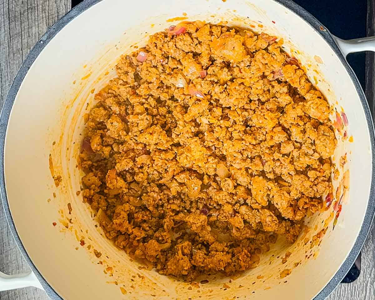A pot of browned sausage crumbles sizzling on the stove.