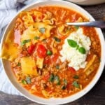 A dinner bowl filled with a hearty serving of lasagna soup, topped with creamy cheese mixture and fresh basil.