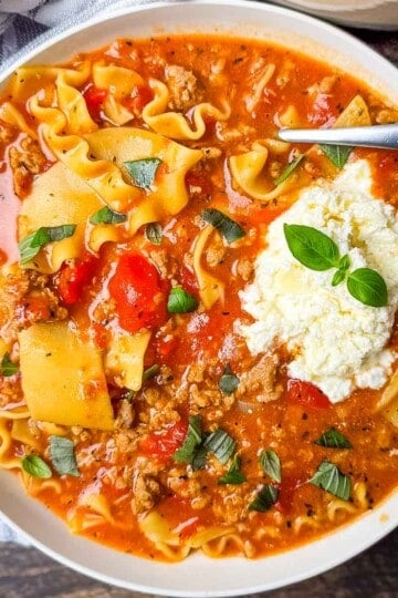 A dinner bowl filled with a hearty serving of lasagna soup, topped with creamy cheese mixture and fresh basil.