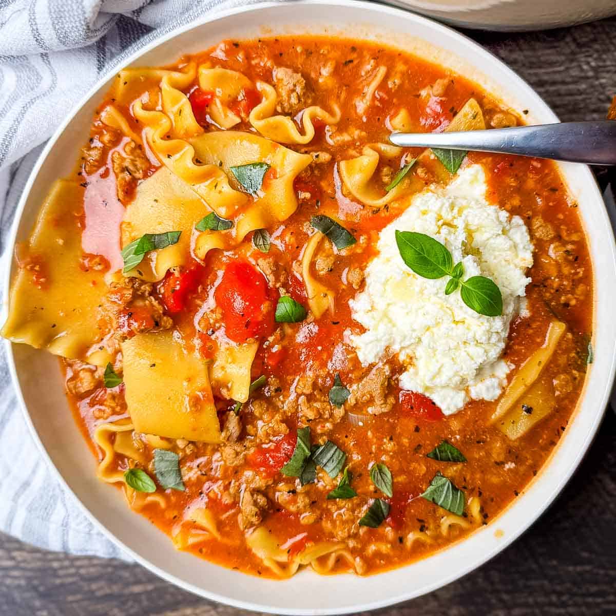 A dinner bowl filled with a hearty serving of lasagna soup, topped with creamy cheese mixture and fresh basil.